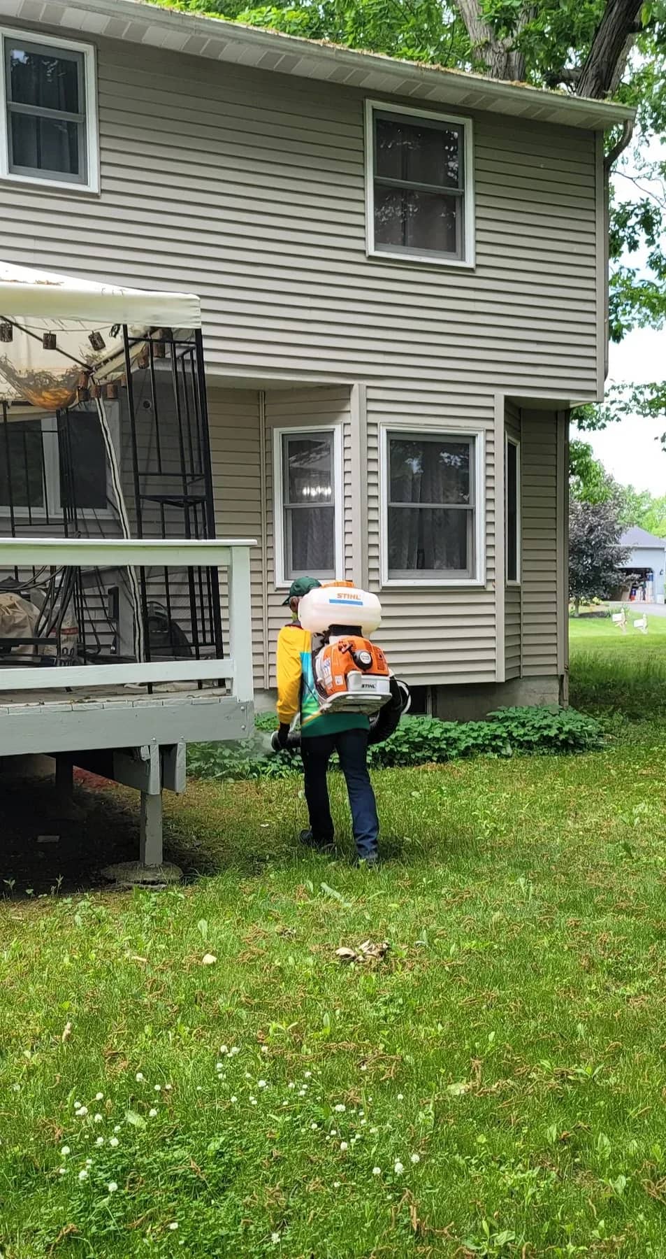 A technician applying a mist treatment to the shrubs beside a client's deck and yard.