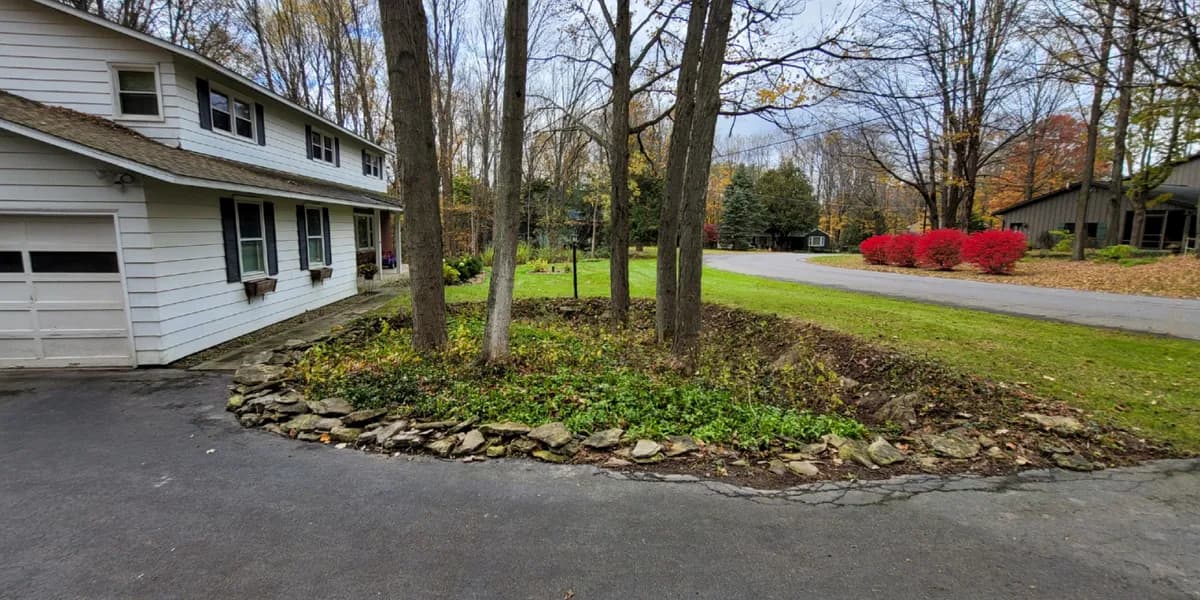 A planting bed between the driveway and the lawn. After: The same bed cleared of leaves, its stone edging and ground cover showing, beside the driveway.